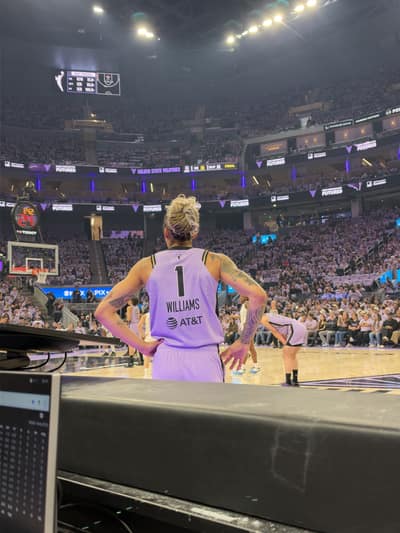 Courtside view of a basketball player in a lavender number 1 jersey with Williams on the back, standing with hands on hips in a packed arena.