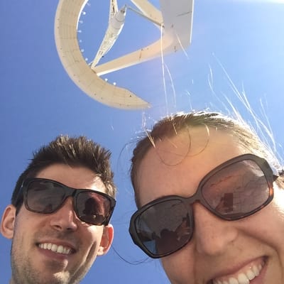 Two people wearing sunglasses take a selfie in front of a large white