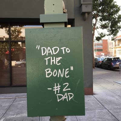 A green street sign with white text reading "DAD TO THE BONE" and "#2 DAD"