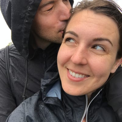 A couple embraces outdoors in the rain, with the man kissing the woman's