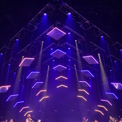 A live music performance takes place on stage beneath a dramatic geometric