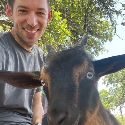 A smiling man in a gray t-shirt poses for a selfie with a brown and black