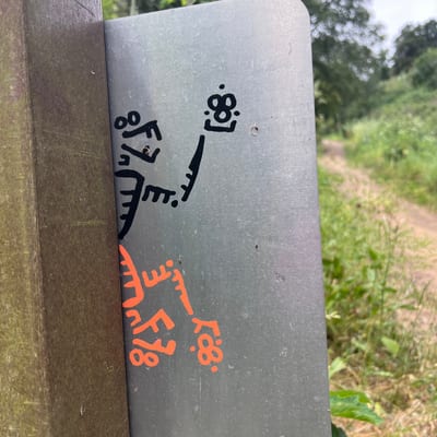 A metal signpost displays black and orange graffiti or stickers in an