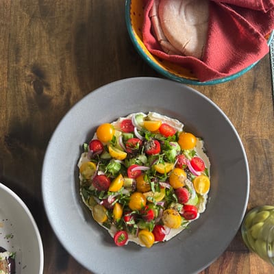 A colorful salad with cherry tomatoes, fresh herbs, and other vegetables is