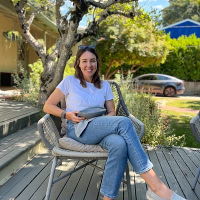 A woman in a white t-shirt and jeans sits smiling in a wicker chair on a