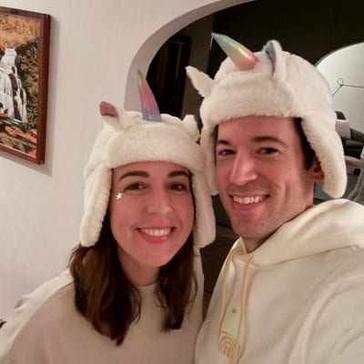 Two people wearing matching white unicorn hats with ears and horns smile at