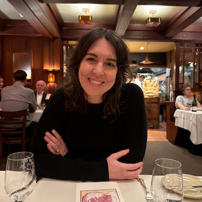 A woman in a black sweater sits smiling at an upscale restaurant table with