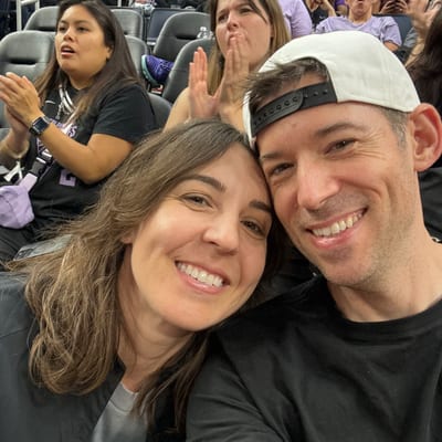 A smiling couple takes a selfie together at what appears to be a sporting