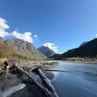 A river winds through a mountainous valley with snow-capped peaks under a
