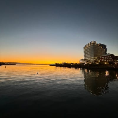 A modern waterfront building complex reflects in calm waters during sunset,