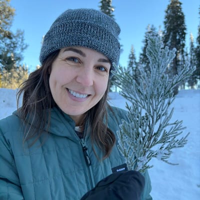 A smiling woman in winter clothing and a knit beanie holds a snow-covered