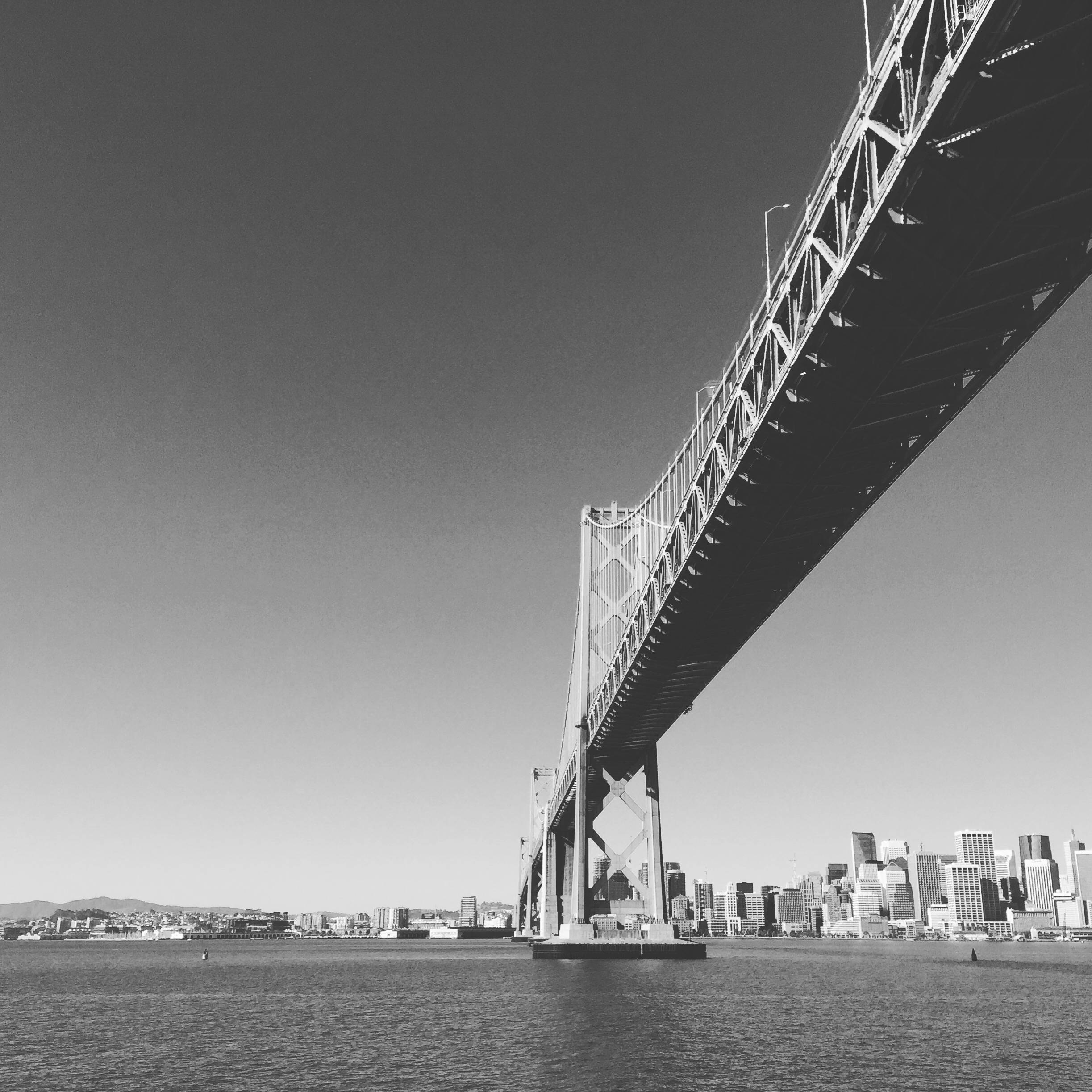 A large suspension bridge spans across a bay with a city skyline of tall