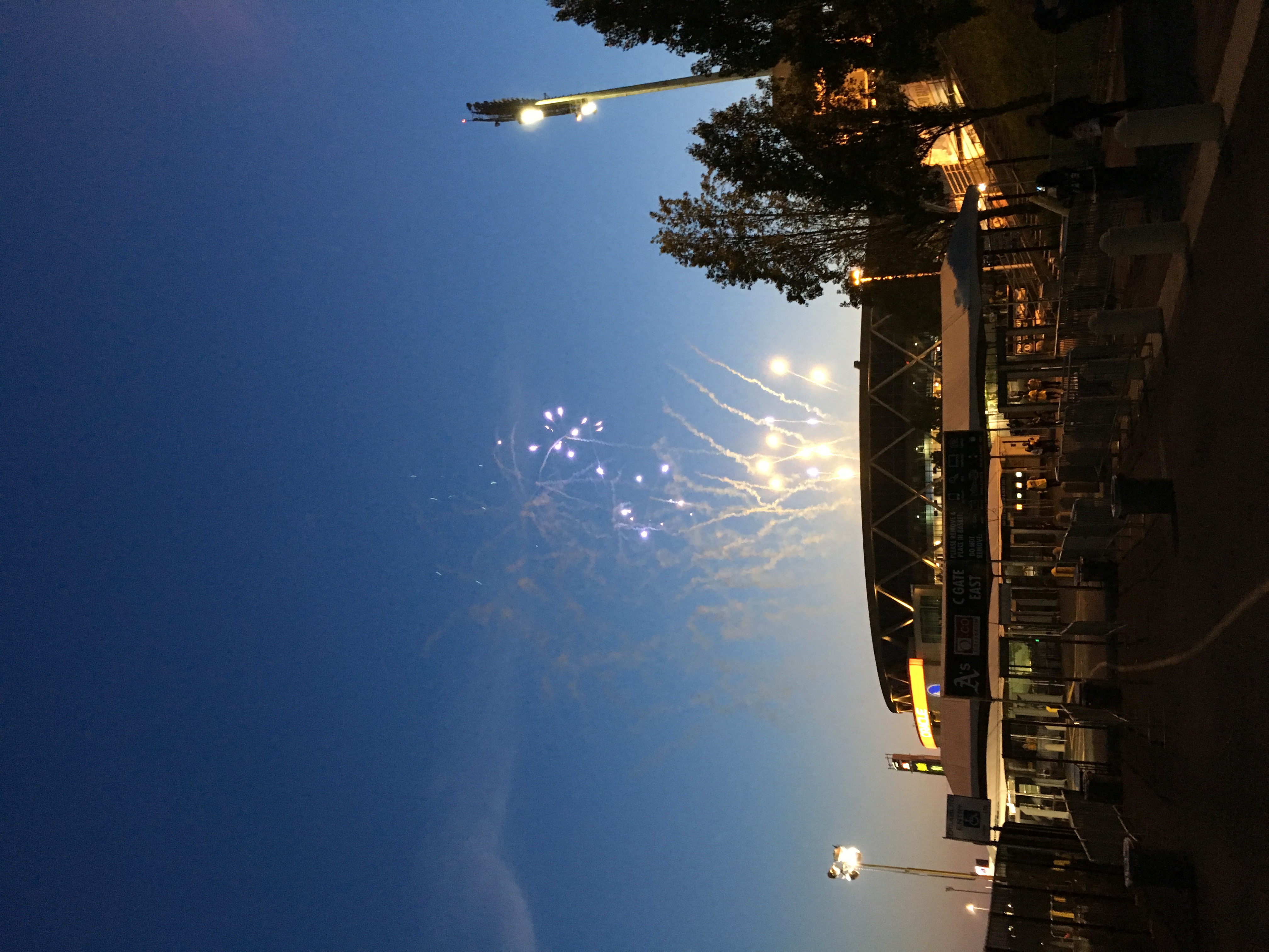 Fireworks explode in the twilight sky above a modern stadium with