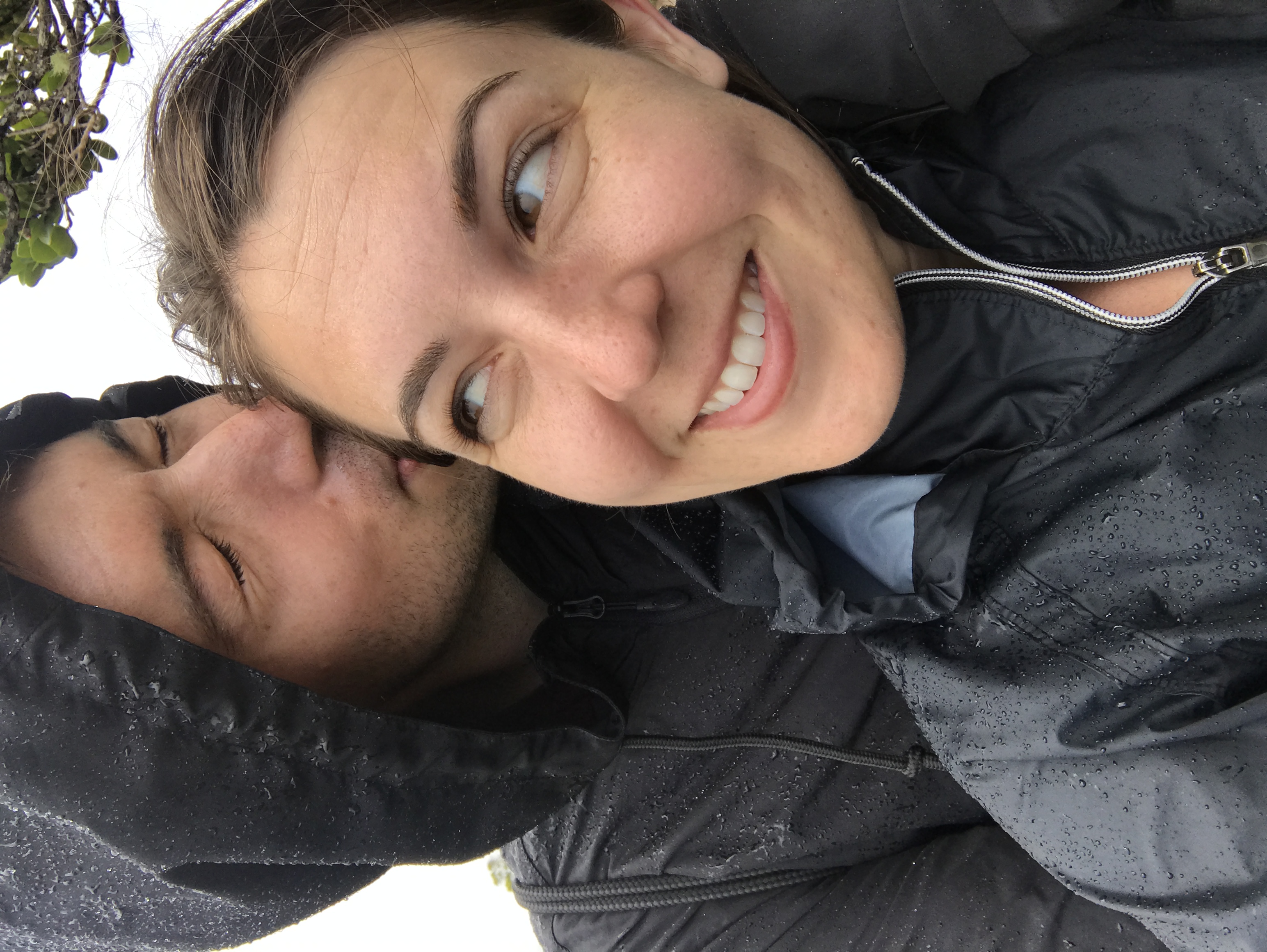 A couple embraces outdoors in the rain, with the man kissing the woman's
