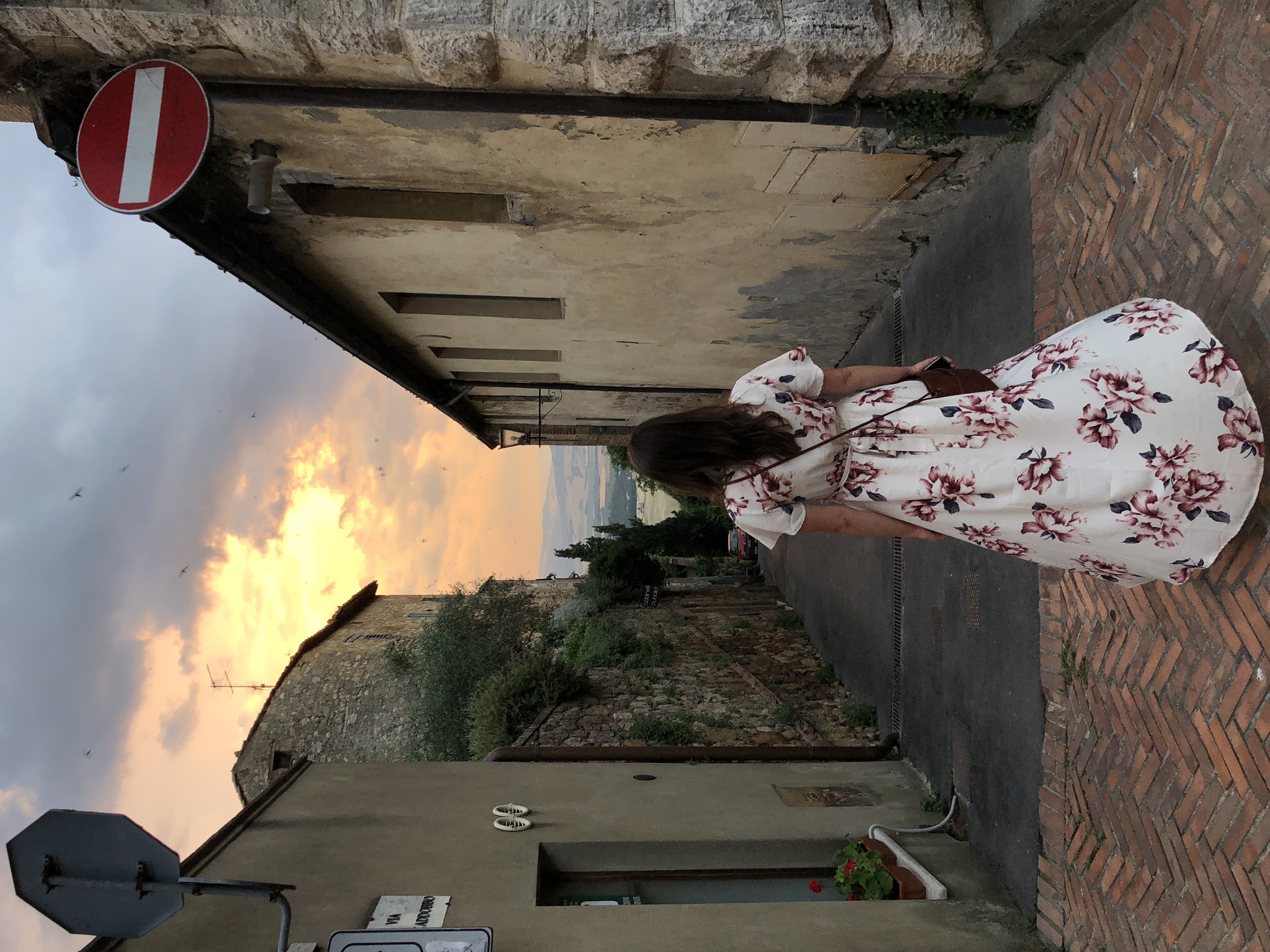 A woman in a white floral dress walks down a narrow cobblestone street in a