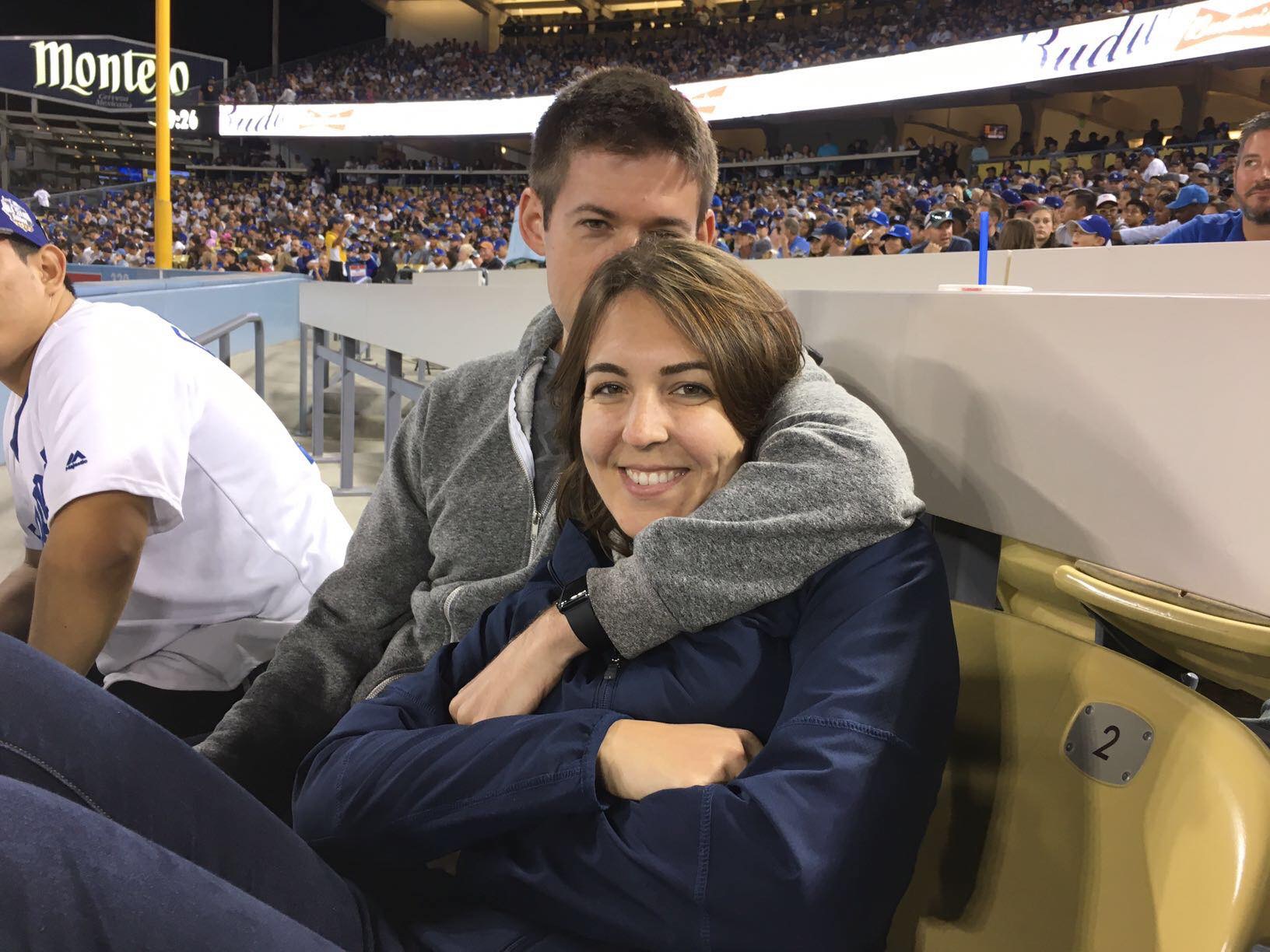 A couple sits close together in stadium seats at a baseball game, with the