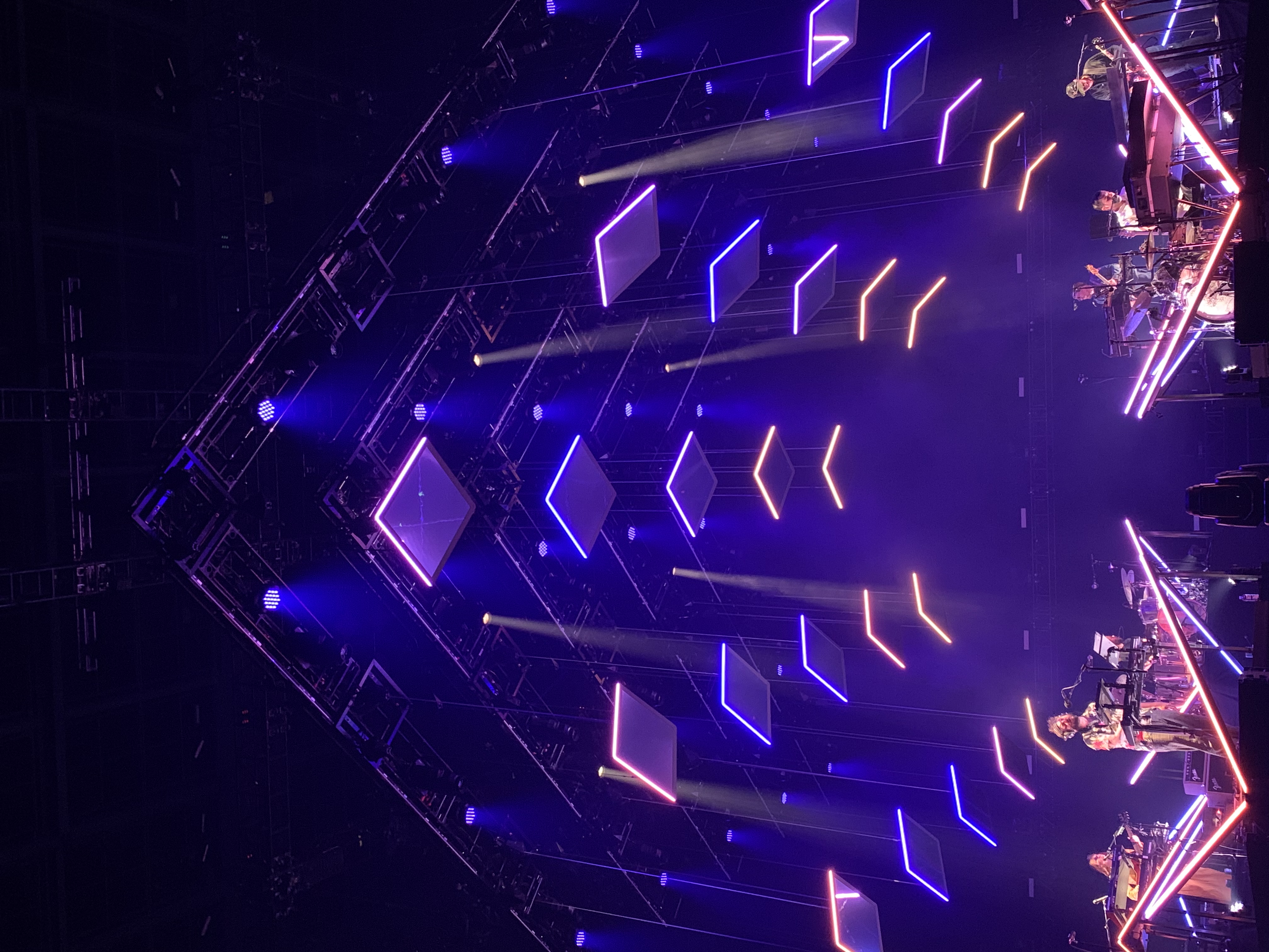 A live music performance takes place on stage beneath a dramatic geometric