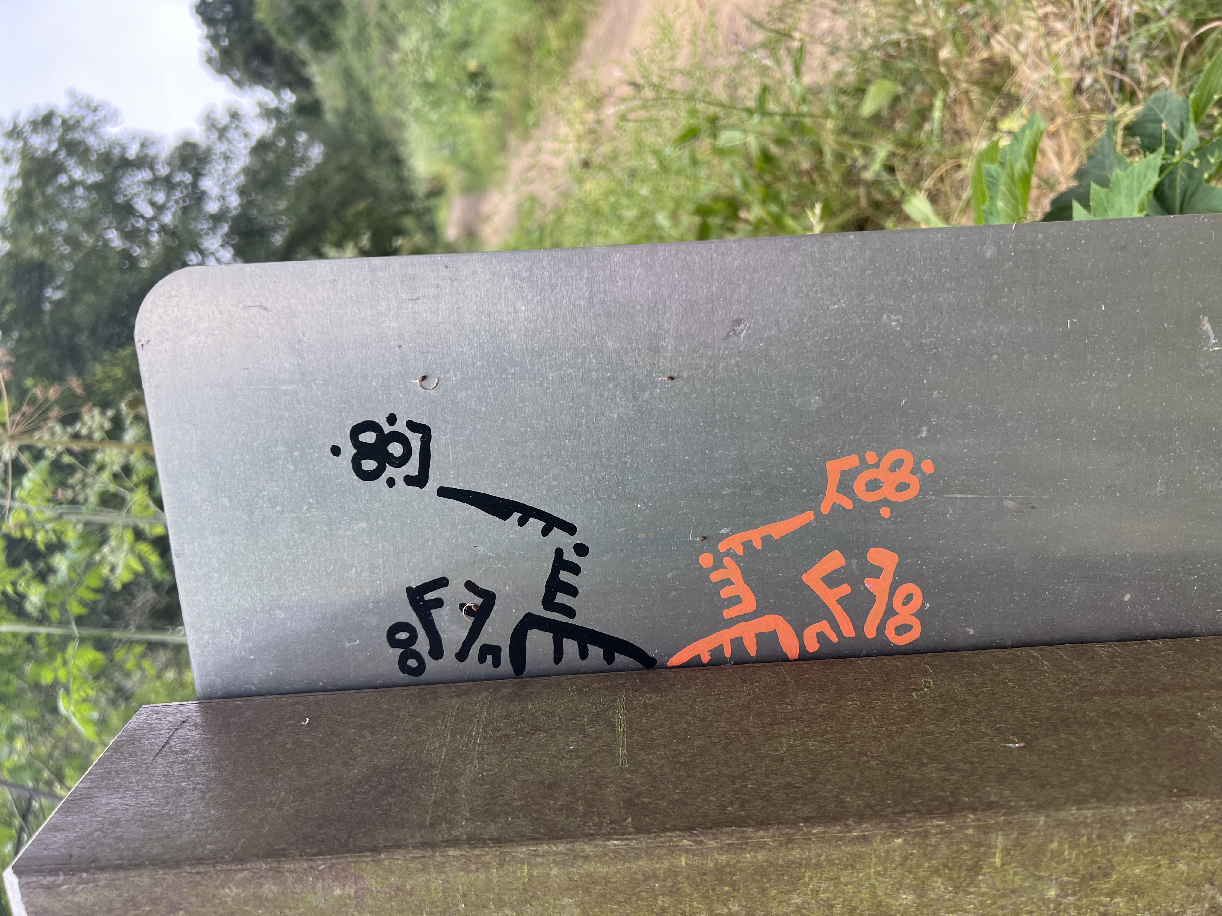 A metal signpost displays black and orange graffiti or stickers in an