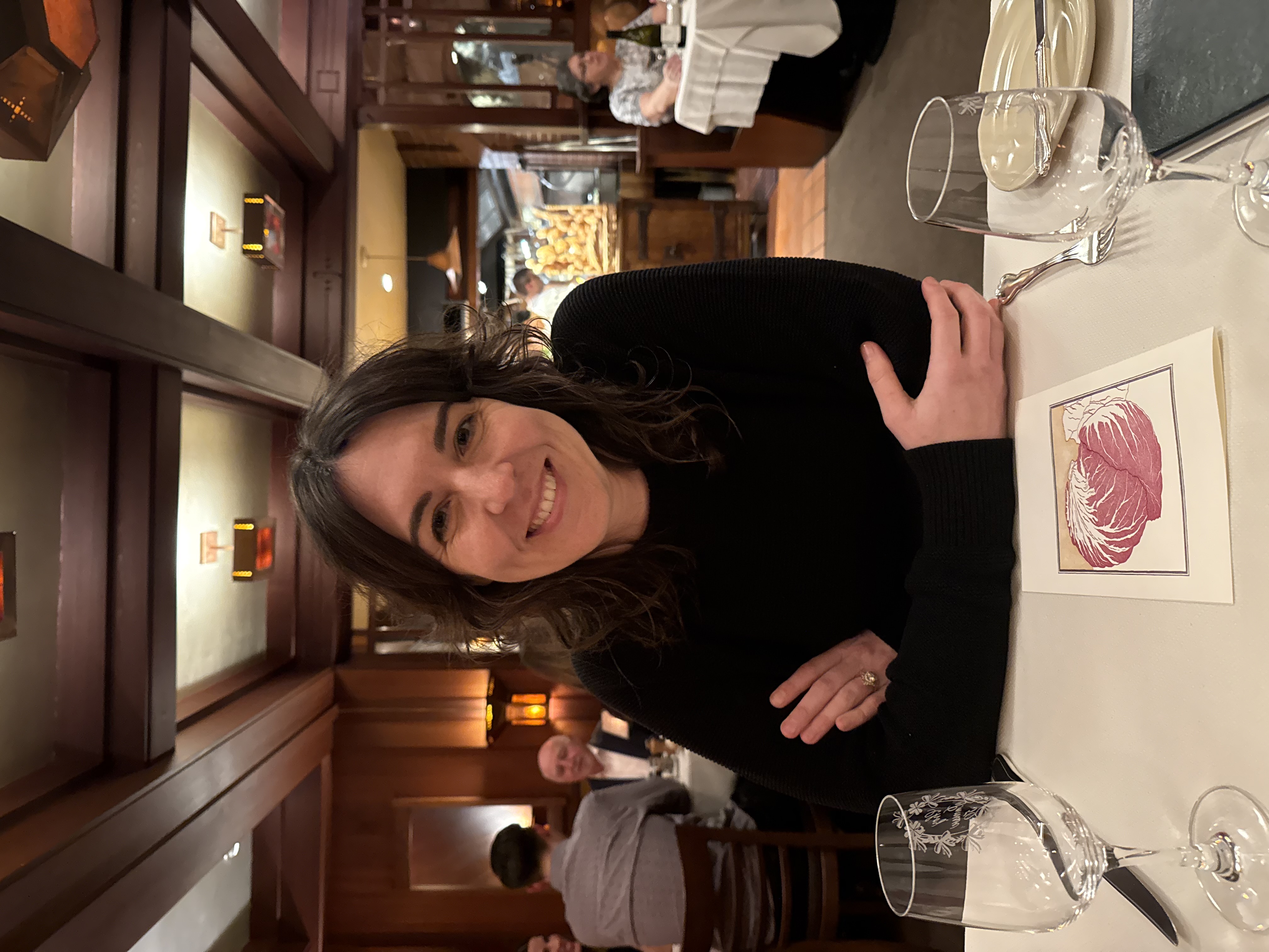 A woman in a black sweater sits smiling at an upscale restaurant table with