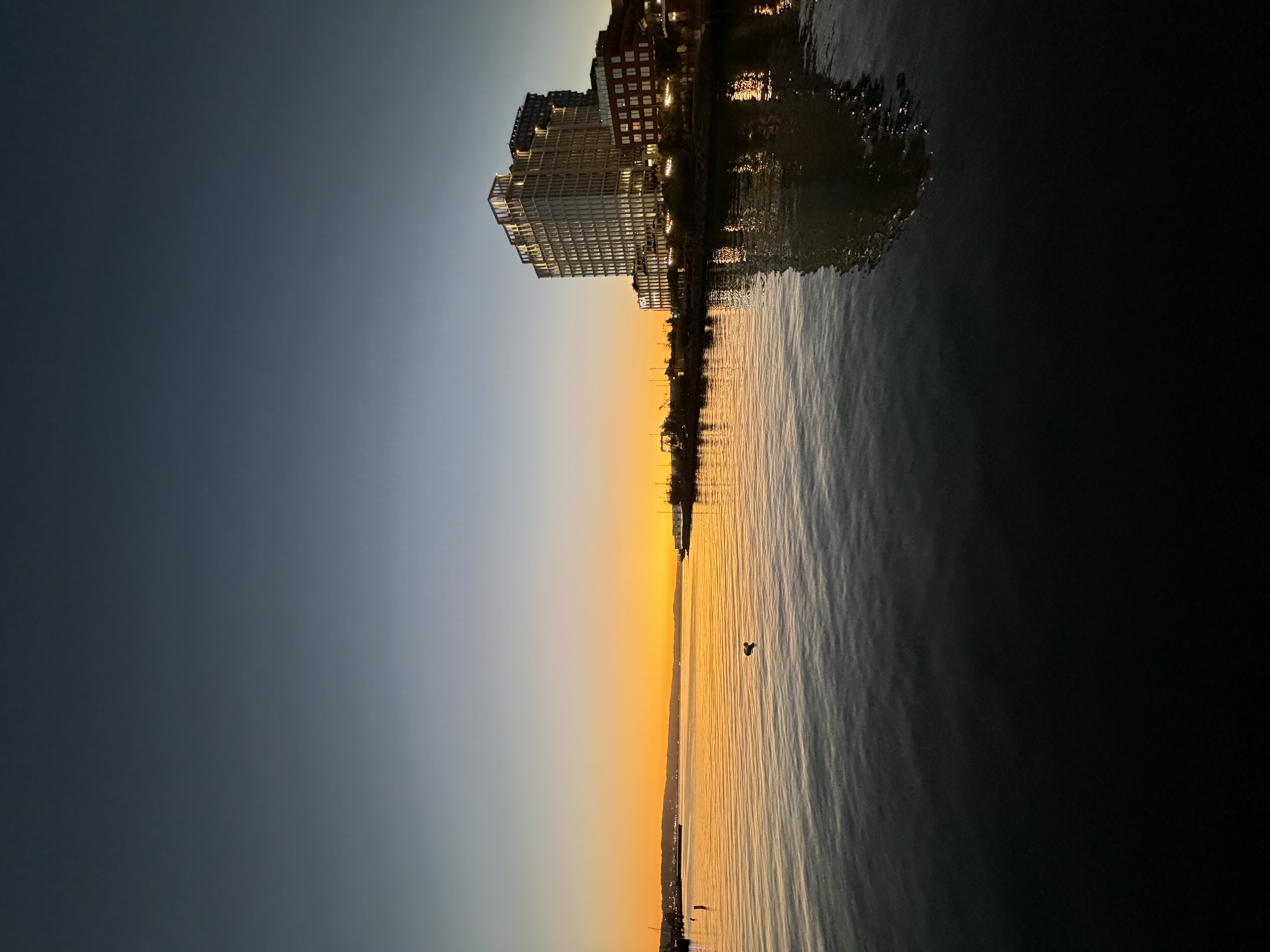 A modern waterfront building complex reflects in calm waters during sunset,